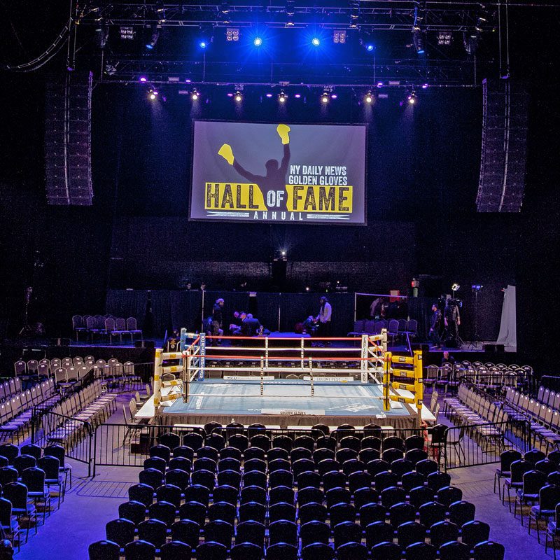 GoldenGloves A boxing ring set in a spacious arena, featuring a large screen above for displaying event details.